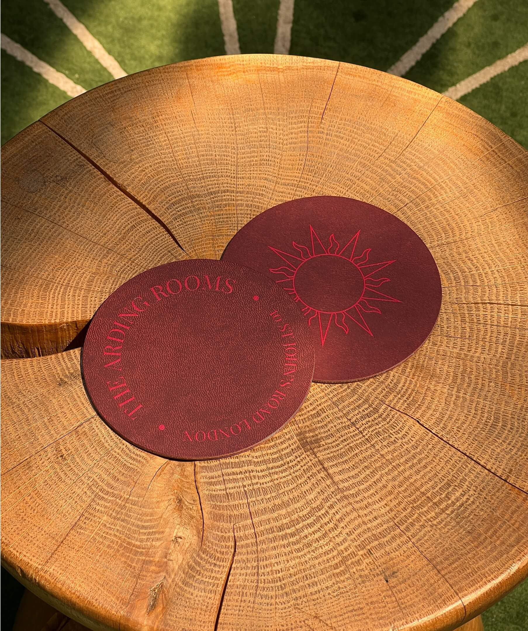 Two red coasters embossed with The Arding Rooms branding, resting on a wooden table