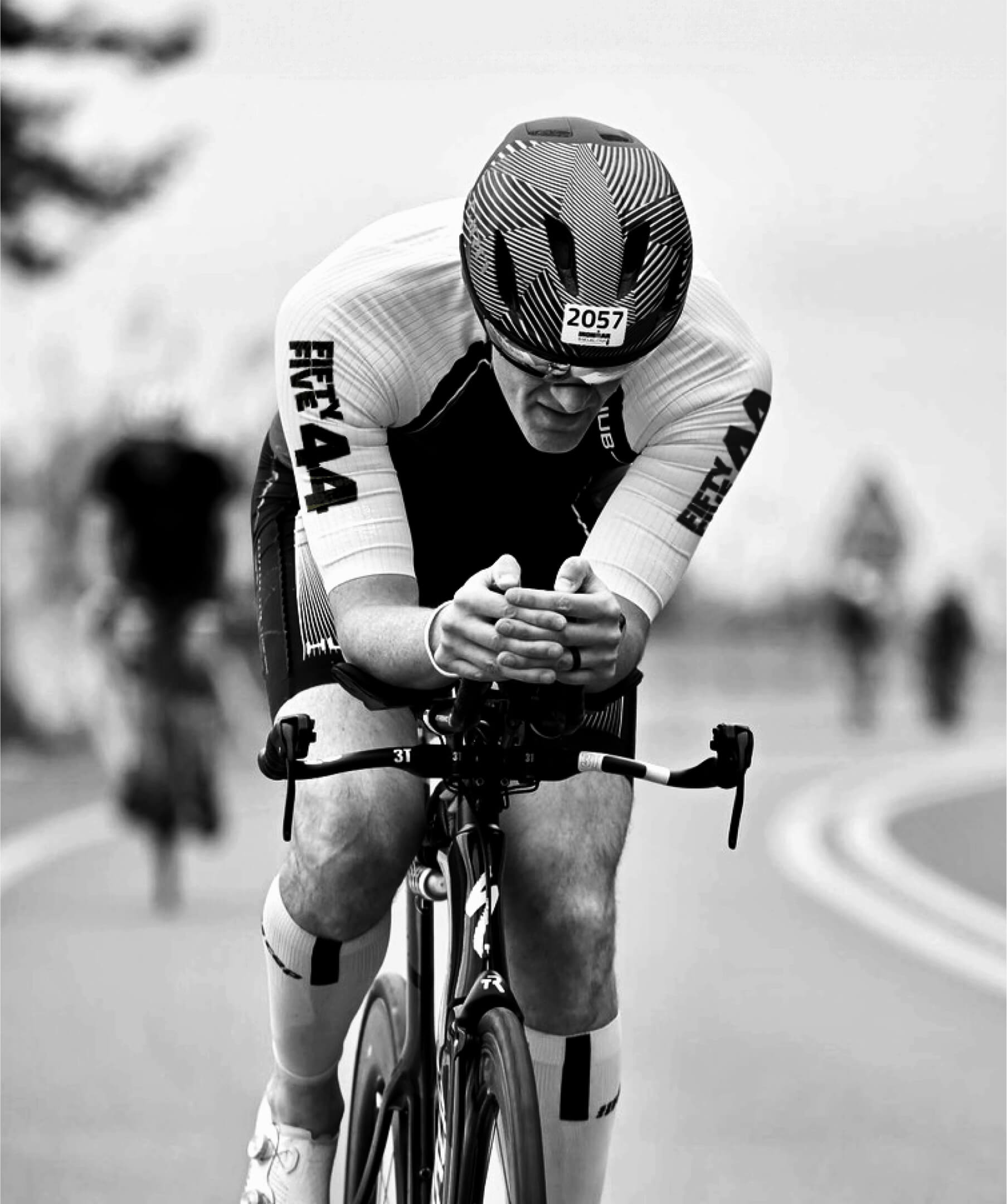 Black and white photo of triathlete cycling, wearing FiftyFive44 branded race suit