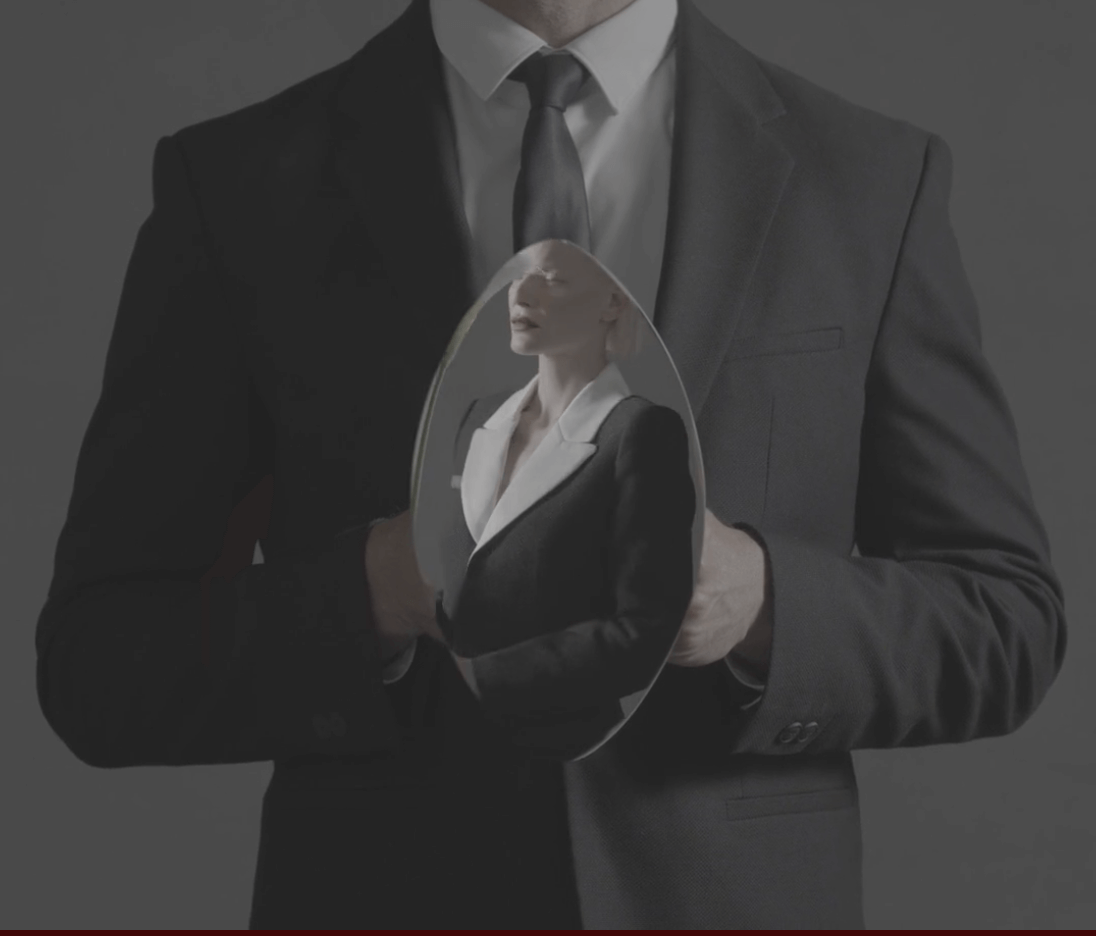 A man in a suit holding a curved reflective mirror that reveals the portrait of a woman inside it